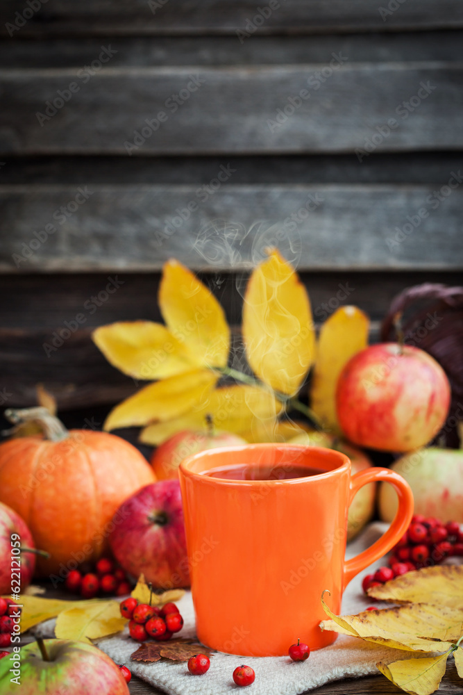 Orange mug on autumn background -fall leaves, apples, pumpkin and rowan-berry Orange mug on autumn background -fall leaves, apples, pumpkin and rowan-berry
