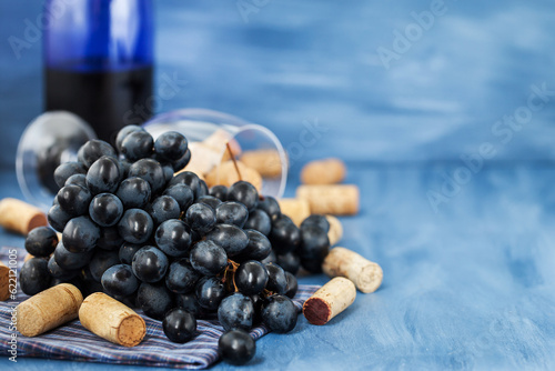 Branch of purple grape and wine corks on the table with glass and bottle on background