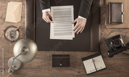 Vintage businessman in the office reading and signing a contract sitting at his desk, top view