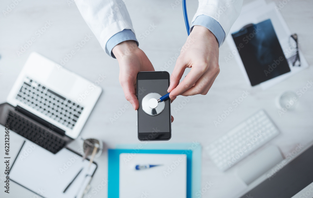Doctor checking heartbeat on mobile phone using a stethoscope, desktop with medical equipment on background, medical app concept Doctor checking heartbeat on mobile phone using a stethoscope, desktop with medical equipment on background, medical app concept