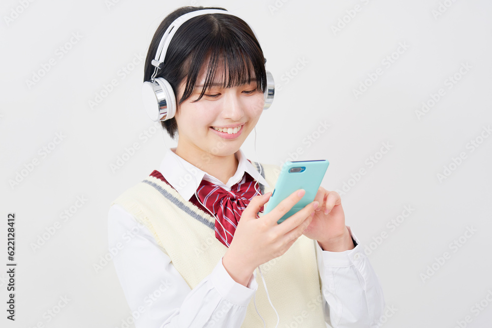 ヘッドホンをしてスマートフォンで音楽を聴く女子高生　白背景