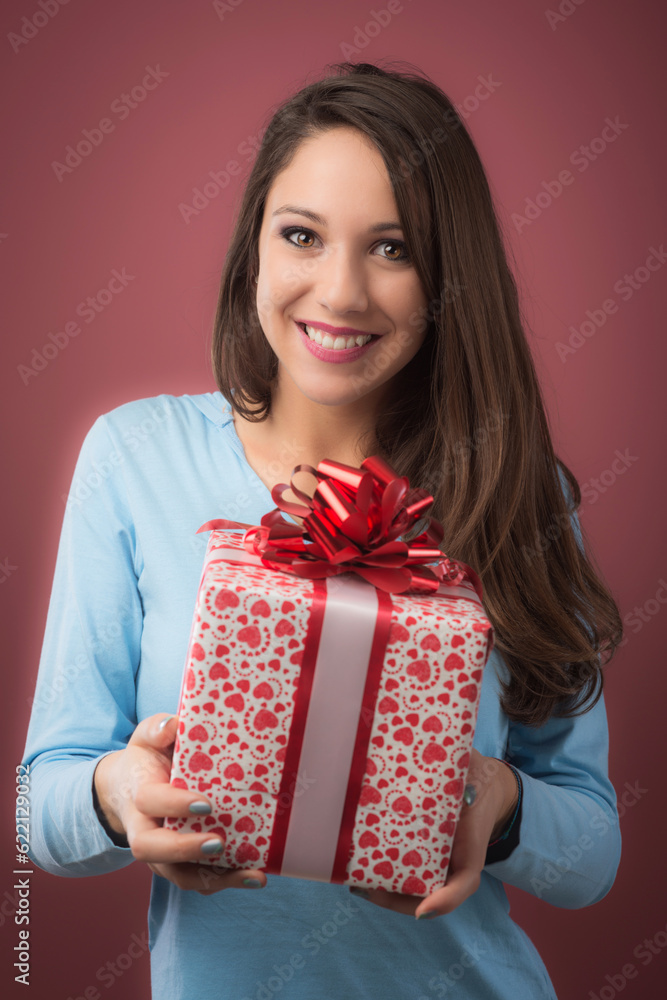 Joyful beautiful young woman holding a gift box with red ribbon Joyful beautiful young woman holding a gift box with red ribbon
