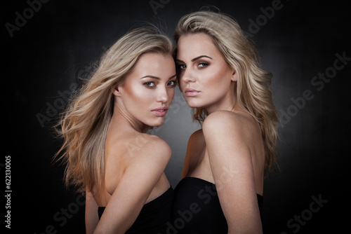 Two sexy girls in casual clothes posing on dark background