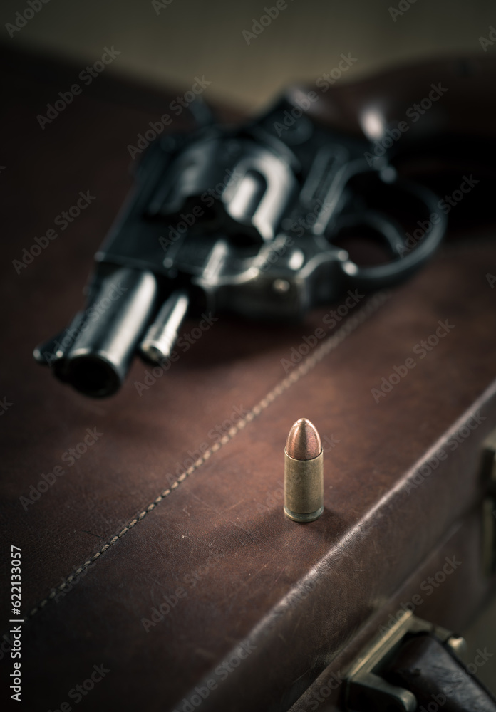 Obraz premium Vintage revolver gun on leather briefcase with bullet close-up.