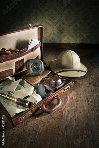 Open leather suitcase with adventurer vintage equipment, including pith hat and brass telescope.