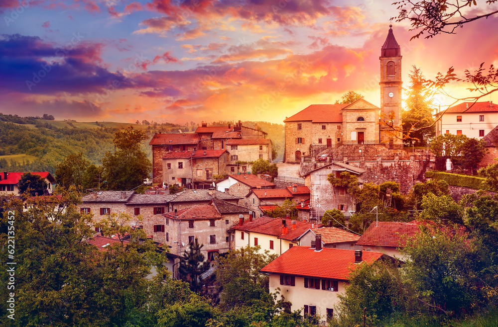 Sunset over old provincial town with Bell tower in Italy red tegular roofs among autumn trees on background dramatic sky clouds