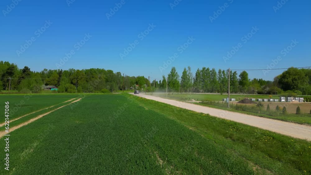 Slow motion of two vehicles driving down a dusty country road next to a field on a clear and sunny summer day. Slow motion of two vehicles driving down a dusty country road next to a field on a clear and sunny summer day.