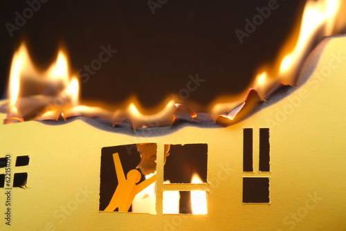 Paper man in window of burning house on dark background photo