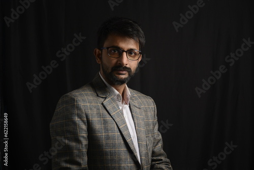 Portrait of happy corporate dressed up person in suit and wearing specs portraying different moods. Low key shoot of bearded office man well suited. Black background.