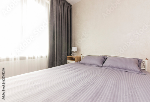 Bedroom with a large bed, two pillows, a bedside table and a curtained window