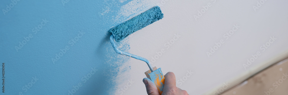 Decorator painting wall with paint roller.