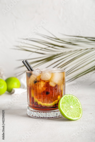 Glass of cold Cuba Libre cocktail and palm leaf on white background