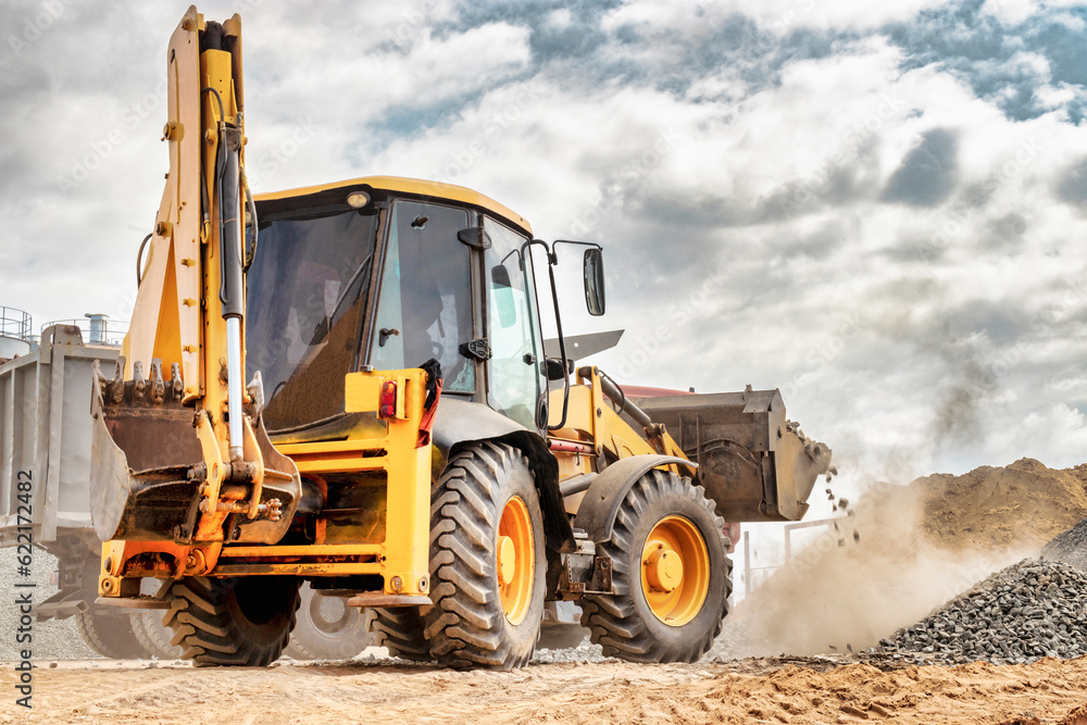 Powerful wheel loader or bulldozer against the sky. Loader transports crushed stone or gravel in a bucket. Powerful modern equipment for earthworks and bulk handling. Powerful wheel loader or bulldozer against the sky. Loader transports crushed stone or gravel in a bucket. Powerful modern equipment for earthworks and bulk handling.