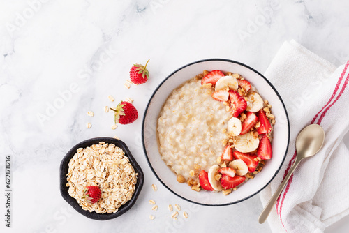 Obraz na plátně Bowl of oatmeal porridge with strawberry and banana on white table top view