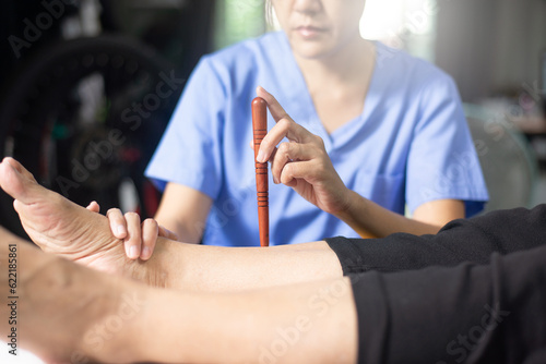 Physiotherapist massaging with wood stick on sick people legs Reflexology spot thai massage.
