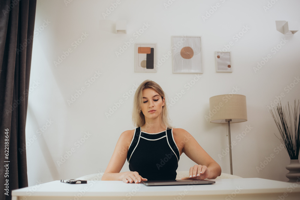Obraz premium Start of a work day. Young woman opening laptop, getting ready for work in the morning at the desk near windows in a beautiful office.