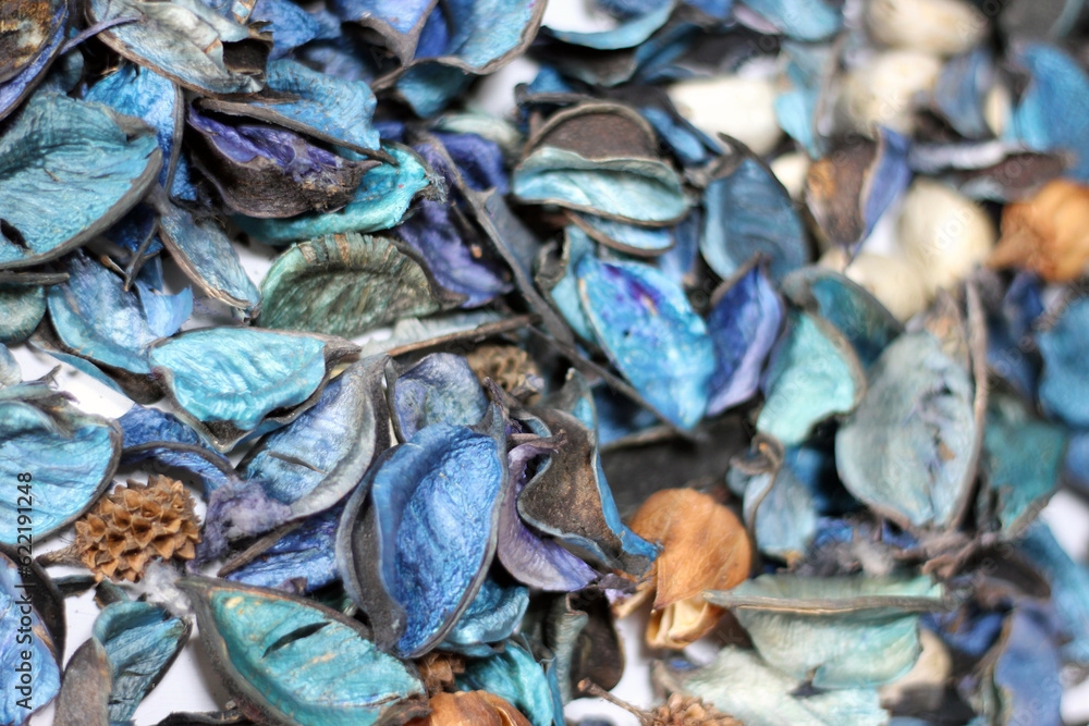 A mix of dry flowers, leaves, petals, and other plant parts. Potpourri background. Purple and blue tone leaves, white color and wood grain background shot.