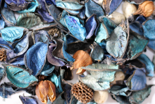 A mix of dry flowers, leaves, petals, and other plant parts. Potpourri background. Purple and blue tone leaves, white color and wood grain background shot.