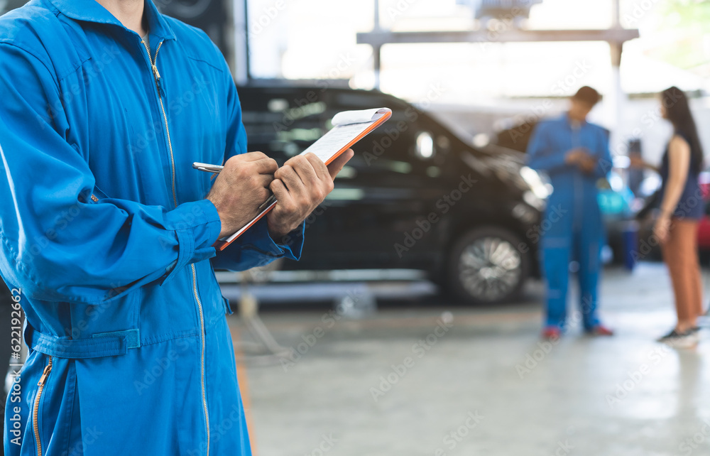 Auto check up and car service shop concept. Mechanic writing job checklist to clipboard to estimate repair quotation to client at workshop garage. Auto check up and car service shop concept. Mechanic writing job checklist to clipboard to estimate repair quotation to client at workshop garage.
