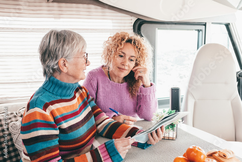 Happy couple of modern women sitting inside a camper van motor home talking looking at map planning the journey. Free lifestyle and travel vacation journey concept photo