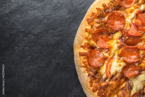 Top view of pepperoni pizza on a black slate plate with copy space for text.