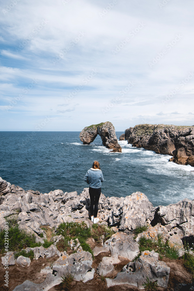 young woman observing the Castro de las Gaviotas from the cliffs of Huelga beach on the Asturian coast, near LLanes