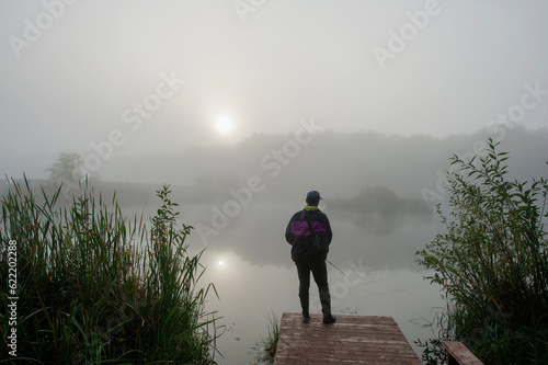 a fisherman on the shore of a pond pulls a spinning fish on a cloudy day