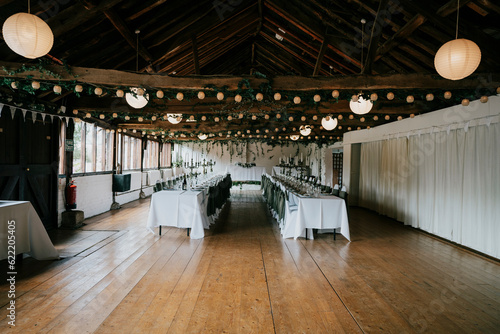 A long wedding hall having two long tables with chairs and wooden floor and ceiling.
 photo