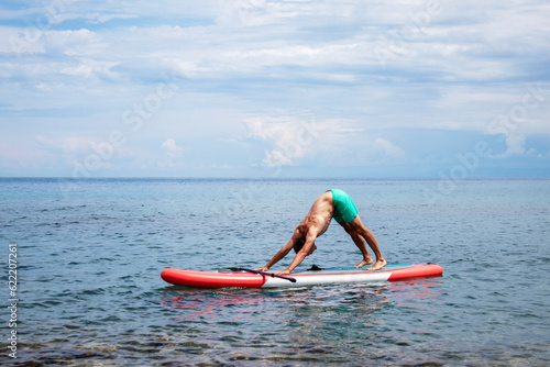 Yoga on the surf with a paddle. Adho mukha shvanasana on surf boards. A man does an asana dog face down photo