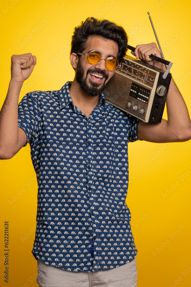 Indian man using retro tape record player to listen music, disco dancing of favorite track, having fun, entertaining, fan of vintage technologies. Handsome hindu guy isolated on yellow background Indian man using retro tape record player to listen music, disco dancing of favorite track, having fun, entertaining, fan of vintage technologies. Handsome hindu guy isolated on yellow background