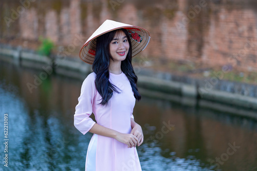 Beautiful Vietnamese women in traditional costumes of Vietnam culture or national costumes wearing hats against an old brick wall. Ao dai is long-dress Vietnamese traditional costume of Vietnamese