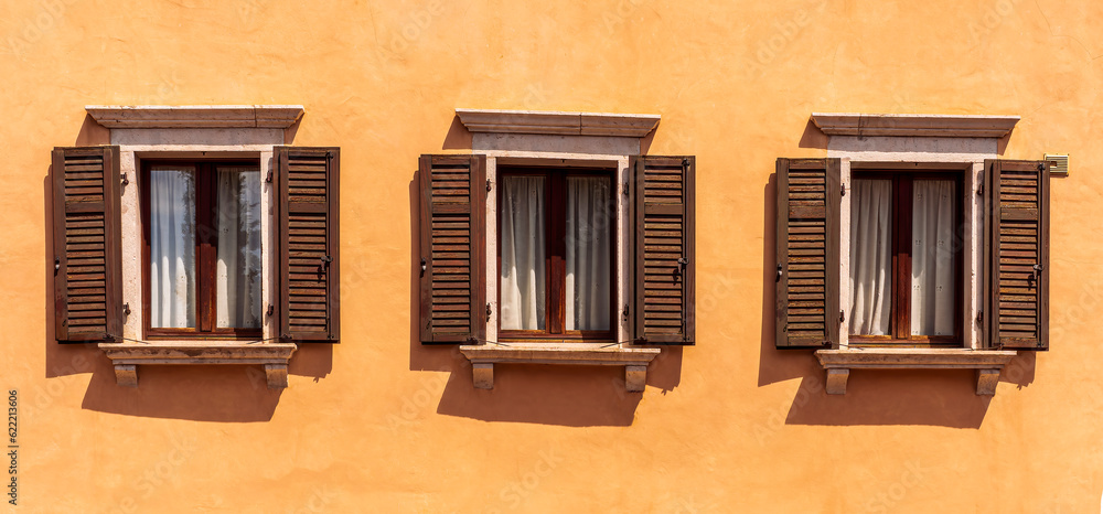 old yellow facade of house with three brown vintage wooden windows in retro italian european style