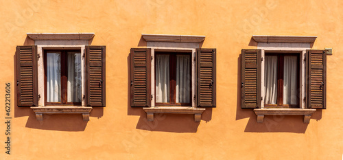 old yellow facade of house with three brown vintage wooden windows in retro italian european style © Yaroslav