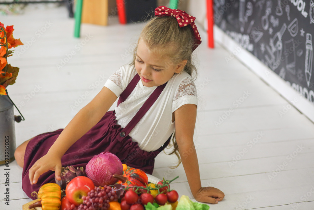 Fototapeta premium Little cute schoolgirl sitting in the classroom. Study of vegetables and fruits. Children. Elementary school. Education concept.