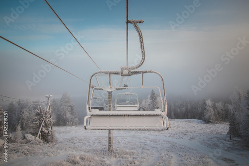 Sunrise breaking through the thick white fog at the top of Vuokatti Hill, a ski resort in Vuokatti, Finland. A view of the frozen chairlift. The Scandinavian experience of winter photo