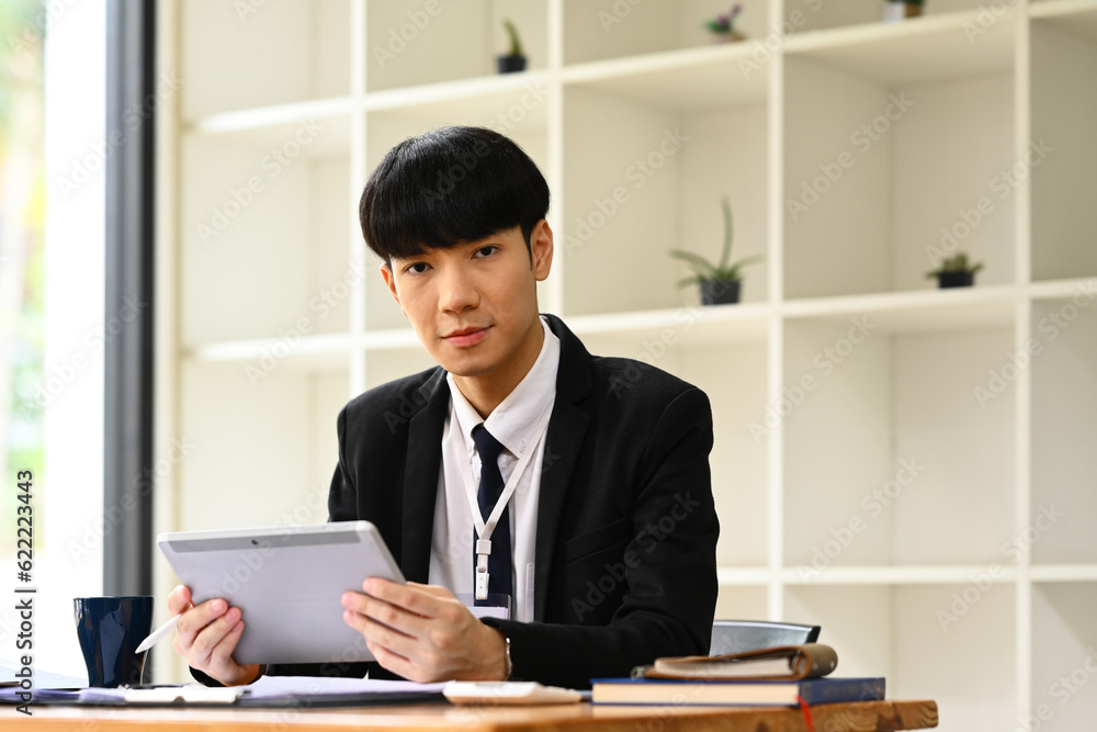 Handsome young businessman in black suit sitting in modern workplace and using laptop and working on marketing projects Handsome young businessman in black suit sitting in modern workplace and using laptop and working on marketing projects