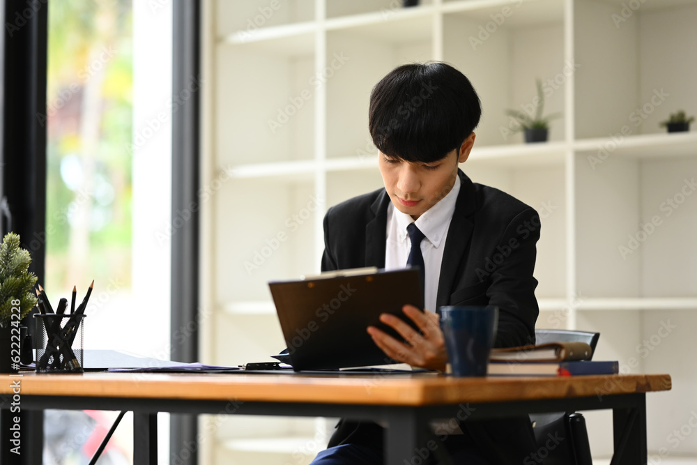 Handsome young businessman in black suit sitting in modern workplace and using laptop and working on marketing projects Handsome young businessman in black suit sitting in modern workplace and using laptop and working on marketing projects