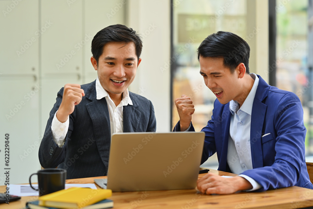 Happy business people looking at laptop screen excited by good news online, celebrating success raising hands up Happy business people looking at laptop screen excited by good news online, celebrating success raising hands up