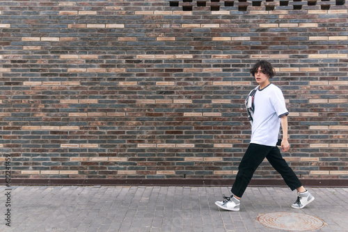 young man walks down the street in front of a brick wall © Evgeny
