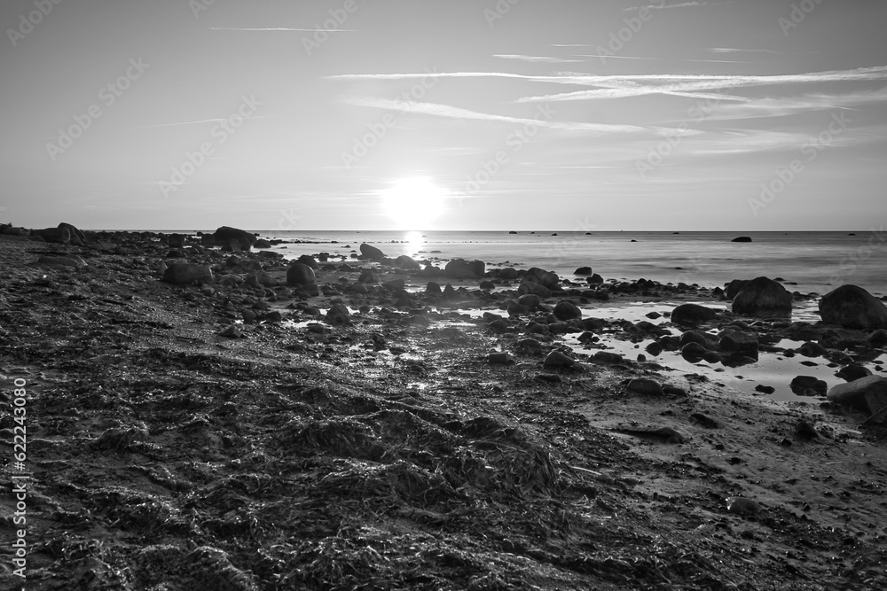 Sunset, stone beach with small and large rocks in black and white.