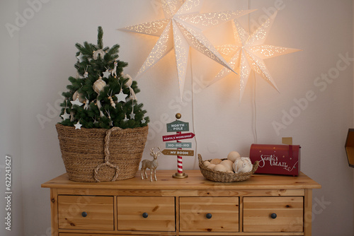 Christmas tree in wicker basket on chest of drawers with decoration
