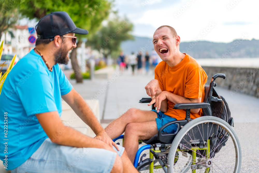 A disabled person in a wheelchair with a friend on summer vacation having fun laughing a lot by the sea