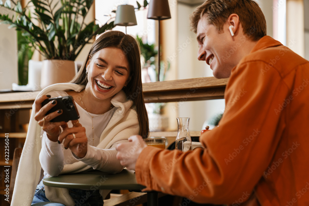 Cheerful couple watching video with smartphone while sitting in cafe Cheerful couple watching video with smartphone while sitting in cafe