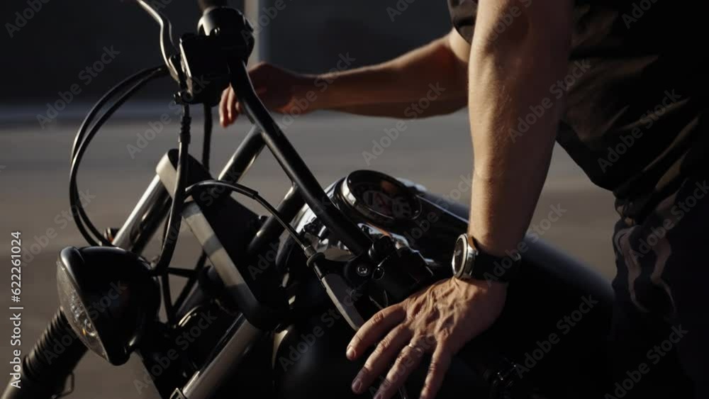 Chrome parts of the bike. A motorcyclist checks the ignition in a black and chrome motorcycle. A protective helmet and black goggles worn by the biker. Chrome parts of the bike. A motorcyclist checks the ignition in a black and chrome motorcycle. A protective helmet and black goggles worn by the biker.