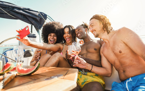 Happy multiracial friends taking selfie while drinking champagne on sail boat - Summer vacation, party and travel concept - Focus on center people faces
