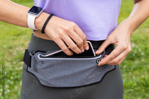 Fitness runner woman getting ready for running with smartwatch and smartphone holder fanny pack waist belt. Athlete woman wearing wearable tech activity tracker for sport exercise activity.