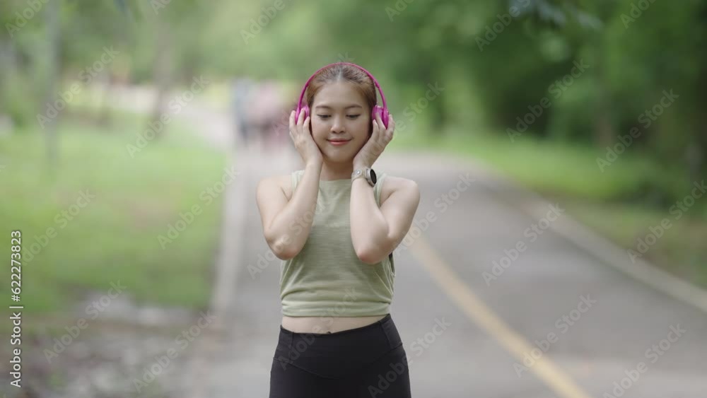 Portrait of smiling beautiful female jogging in the park listening to music with pink headphone Portrait of smiling beautiful female jogging in the park listening to music with pink headphone