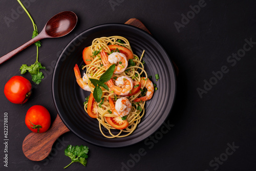 Stir-fried spaghetti or stir-fried noodles Tomato sauce and prawns on a black plate On a wooden table background. Top view.