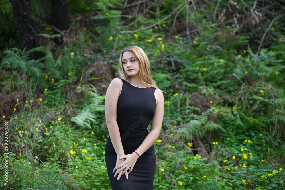 Young, beautiful blonde woman dressed in black walks through the forest in different postures and expressions. In the background ferns and yellow flowers. Concept expressions in nature. Young, beautiful blonde woman dressed in black walks through the forest in different postures and expressions. In the background ferns and yellow flowers. Concept expressions in nature.