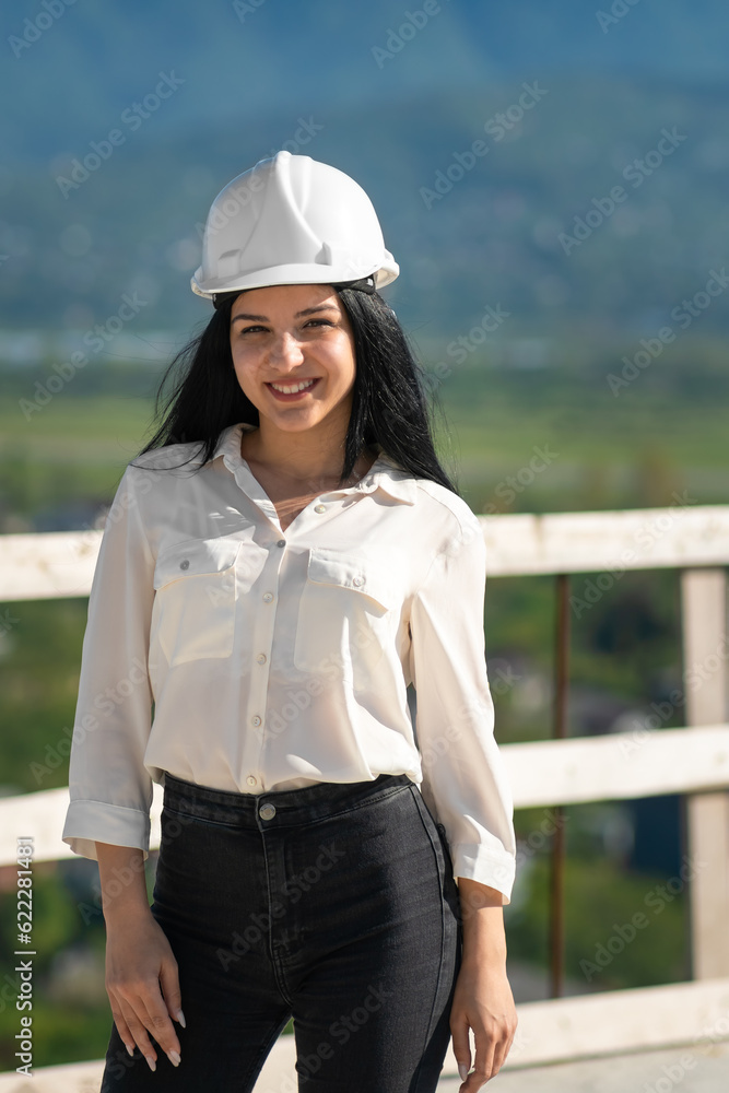 Young smiling female engineer in a hard hat on a construction site looks into the camera. Supervisor wearing a protective helmet while working on a construction site Young smiling female engineer in a hard hat on a construction site looks into the camera. Supervisor wearing a protective helmet while working on a construction site